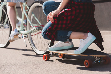 cropped shot of woman riding bicycle and towing her female friend on skateboard
