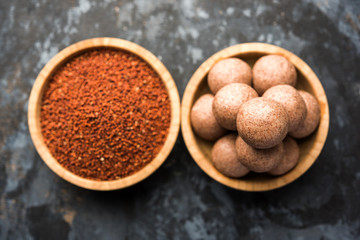 Nachni laddu or Ragi laddoo or balls made using  finger millet, sugar and ghee. It's a healthy food from India. Served in a bowl or plate with raw whole and powder. Selective focus