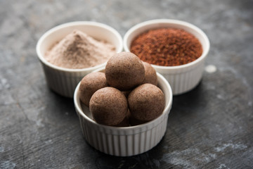 Nachni laddu or Ragi laddoo or balls made using  finger millet, sugar and ghee. It's a healthy food from India. Served in a bowl or plate with raw whole and powder. Selective focus