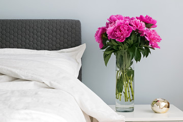 Bed with white bed sheets and pink peonies on the nightstand.