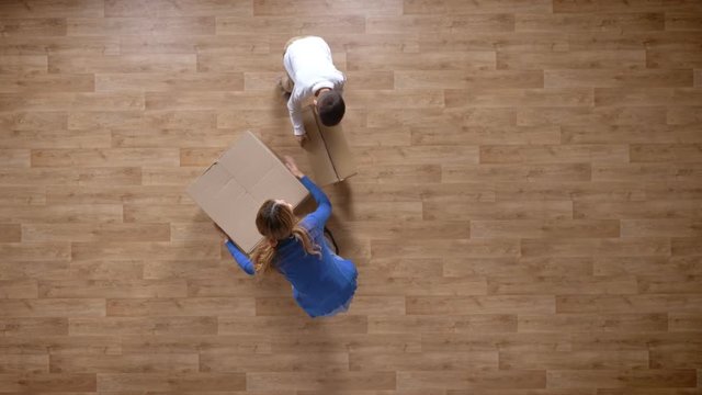 Young mother and son coming into empty house with boxes, top shot, little boy running and hugging mother, parquet wooden floor