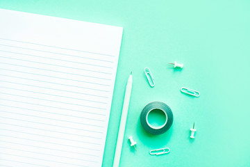 Beautiful office stationery flatlay with ruled notebook, pen and paper clip on the bright desk with turquoise background.