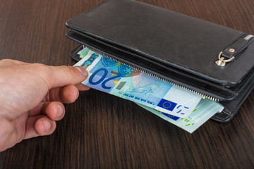 Male hand holding a leather wallet and withdrawing European currency Euro EUR