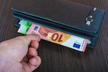 Male hand holding a leather wallet and withdrawing European currency Euro EUR