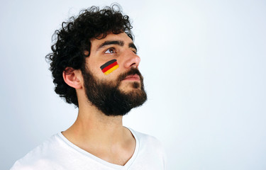 Sport fan head high and feeling proud when listening to the anthem of his country. Man with the flag of Germany makeup on his face and white t-shirt.  