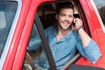 handsome smiling man sitting in red car during road trip