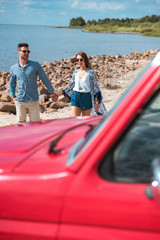 Fototapeta premium young couple holding hands and walking on shore near the sea during road trip