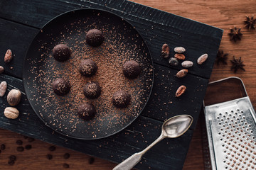 elevated view of cutting board with truffles on plate covering by grated chocolate, spoon, cocoa beans, nutmegs, anise and grater on wooden table