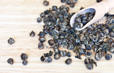 Rolled dry oolong tea leaves in a spoonful and scattered on a wooden table. Traditional Oriental...