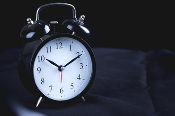Old Black vintage alarm clock on black bedspread.