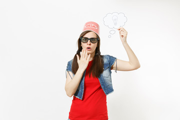 Portrait of Young shocked woman in 3d glasses with bucket for popcorn on head watching movie film, holding say cloud with lightbulb, idea isolated on white background. Emotions in cinema concept.