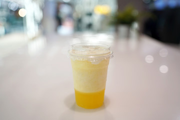 Plastic glass of pineapple smoothie with layer of cream cheese foam on blurred background and copy space, Traditional Taiwanese and Chinese Beverage.