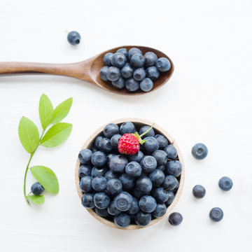Fresh blueberries in a wooden cup and  wooden spoon on a light surface. Closeup, top view.