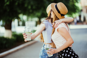Two happy young women hugging and laughing outdoors summer time