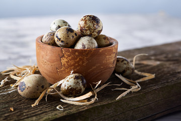 Wooden bowl filled with quail eggs on wooden board over white background, close-up, selective focus.