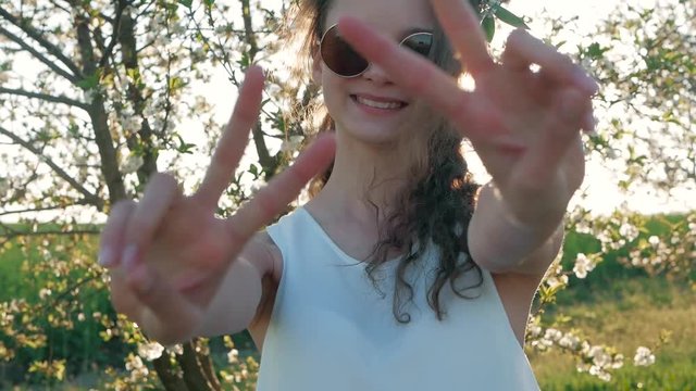 Beauty young woman enjoying nature in spring apple orchard and shows a sign of peace. Happy Beautiful girl in Garden with blooming trees
