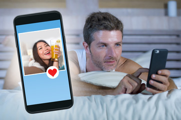 young attractive man lying in bed on line searching for sex or love finding a beautiful girl profile sending like using mobile phone in internet relationship