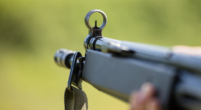 Shotgun in man' s hand. Front side of weapon with close up view on blurred nature background.