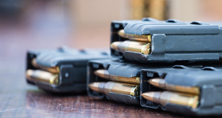 Magazines with bullets of firearm putted on wooden table. Close up view, blurred background. - obrazy, fototapety, plakaty