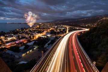 Fototapeta premium Fireworks over light trails of cars on the tamarin road in Saint Paul, Reunion Island
