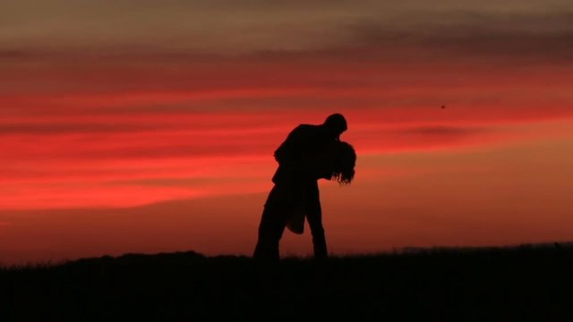 Silhouettes of the adorable couple tenderly kissing while dancing over the red sky during the sunset.