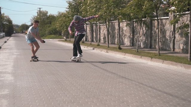 Two hipster skateboarders friends make board tricks and filming them on camera, streeet day slowmotion