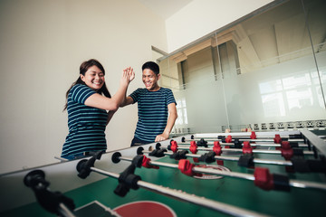 Happy asian family playing table football together in sport club.