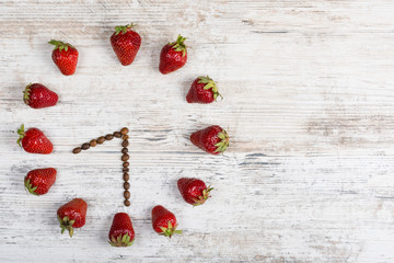 strawberry clock with arrows from coffee beans, showing the time of 8:30 or 20:30 on a wooden antique table in the kitchen