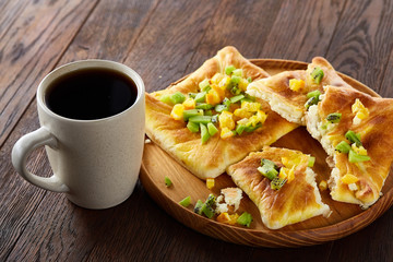 Morning concept with a cup of coffee, breadsticks, fruit pies and oranges on wooden background.