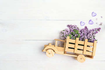 Wooden toy truck with lilac flowers in the back on white wooden background. Space for text.