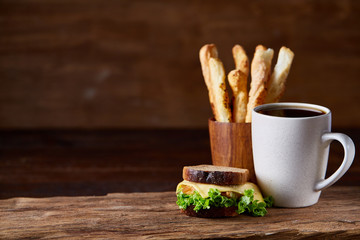 Breakfast table with sandwich and black coffee on rustic wooden background, close-up, selective focus