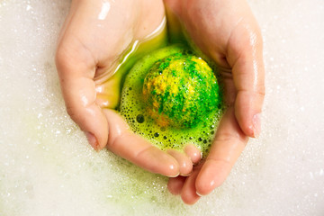 Green bubbling ball of bath salts in hands. Bomb for the bath. Green hands. Green water with foam. Closeup. It dissolves in the hands.