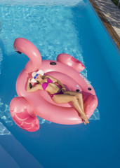 AERIAL: Flying above woman lying on a floatie and sunbathing in middle of pool.