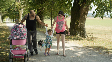 Gentle muscular dad pushing stroller and slim mom lift their little daughter.