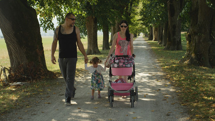 Inked parents take their playful little daughter and newborn girl for a walk