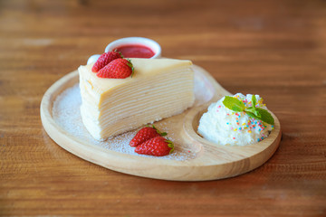 Crepe cake with cream and strawberry fruit on top and  sauce in ceramic cup on wooden plate.