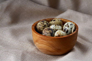 Quail eggs in a wooden bowl on a homespun tablecloth, top view, close-up