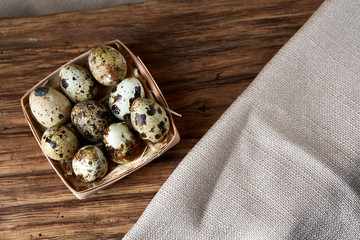 Composition of eggs quail box, eggs on a homespun napkin, boxwood on wooden background, top view