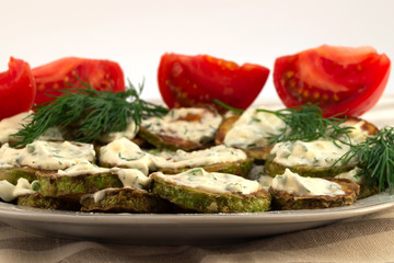 Fried in butter round zucchini slices, smeared with mayonnaise on top, next to dill sprigs and several tomato slices.