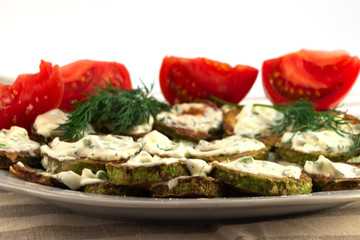 Light snack from roasted zucchini slices with mayonnaise along with dill sprigs and tomato slices.
