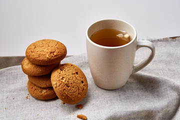 White porcelain mug of tea and sweet cookies on homespun napkin over white background, top view, selective focus