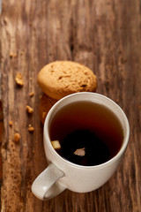 White porcelain mug of tea and sweet cookies on piece of wood over wooden background, top view, selective focus