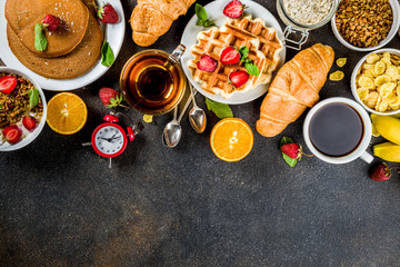 Healthy breakfast eating concept, various morning food - pancakes, waffles, croissant oatmeal sandwich and granola with yogurt, fruit, berries, coffee, tea, orange juice, dark rusty background