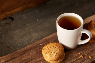 White porcelain mug of tea and sweet cookies on piece of wood over wooden background, top view, selective focus