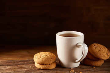 White porcelain mug of tea and sweet cookies on piece of wood over wooden background, top view, selective focus