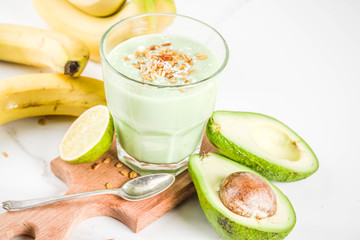 Healthy summer drink, avocado and banana smoothie with lime, granola and coconut milk, dark rusty background copy space
