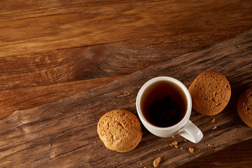 White porcelain mug of tea and sweet cookies on piece of wood over wooden background, top view, selective focus