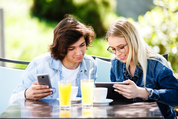 Young couple using tablet and phone while sitting together at cafe