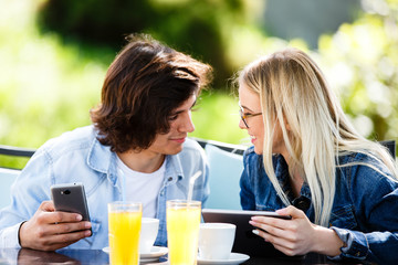 Young couple using tablet and phone while sitting together at cafe