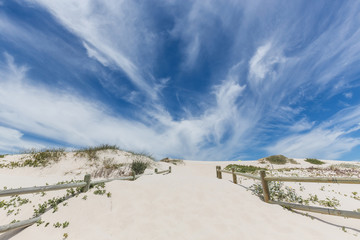Pathway to sandy beach with blue sky